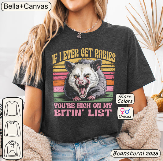 Person wearing a dark gray t-shirt with an opossum graphic and text, with 'Bella+Canvas' branding.