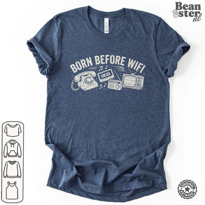 A heather navy blue t-shirt with a white graphic print reading 'BORN BEFORE WIFI' above retro telephone, cassette tape, radio, and TV illustrations. 
