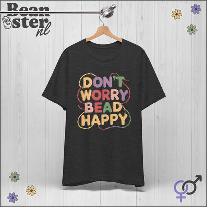 Black t-shirt with colorful text 'Don't Worry Bead Happy' on a wooden background with floral decorations.