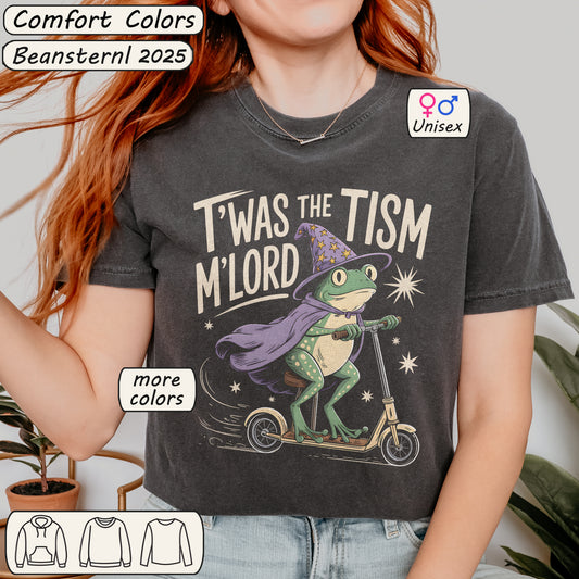 Person wearing a dark gray t-shirt with a graphic of a frog on a scooter and text, T’was The ‘Tism M’lord 