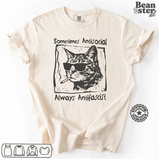 A cream-colored short-sleeve t-shirt with a black graphic print of a cat wearing sunglasses and a cigarette, with the text 'Sometimes Antisocial' above and 'Always Antifascist' below. The t-shirt is laid flat on a white background with a 'Beanster.