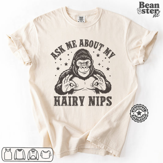 A beige short-sleeve graphic t-shirt laid flat on a white background. The shirt features a black graphic of a gorilla flexing its chest with the text 'ASK ME ABOUT MY HAIRY NIPS' printed around it.