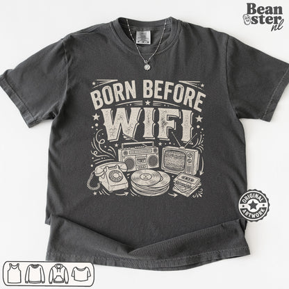 A dark gray graphic t-shirt laid flat on a white background, featuring a white distressed print that reads 'BORN BEFORE WIFI' above retro electronic illustrations.