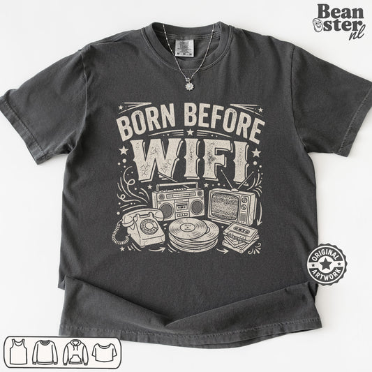 A dark gray graphic t-shirt laid flat on a white background, featuring a white distressed print that reads 'BORN BEFORE WIFI' above retro electronic illustrations.