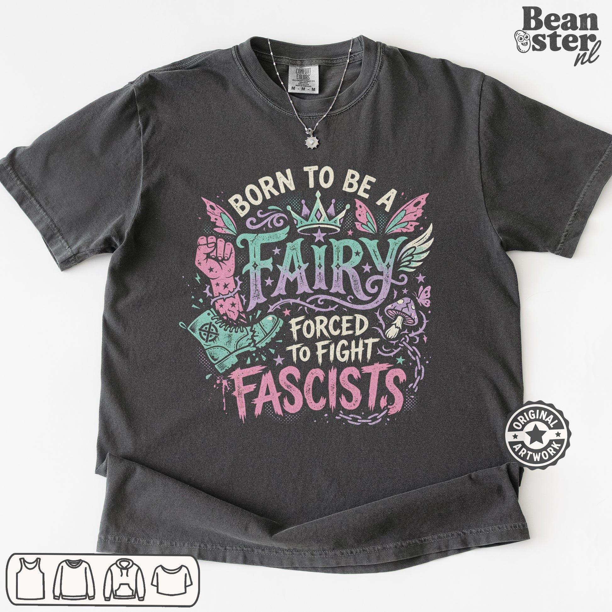 A dark charcoal gray graphic t-shirt laid flat on a white background. The shirt features a colorful graphic with the text 'BORN TO BE A FAIRY FORCED TO FIGHT FASCISTS' in pink, teal, and white.