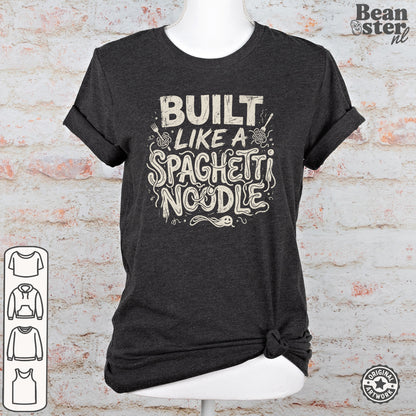 A dark heather gray t-shirt displayed on a white mannequin torso against a white brick wall background. The t-shirt features a distressed cream-colored graphic that reads 'BUILT LIKE A SPAGHETTI NOODLE' with pasta illustrations.