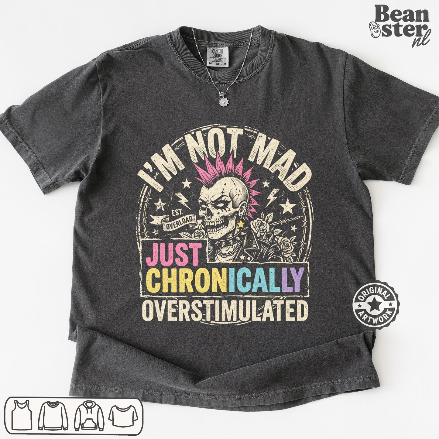 A dark gray graphic t-shirt featuring a skull with pink hair and the text 'I'M NOT MAD JUST CHRONICALLY OVERSTIMULATED'. 