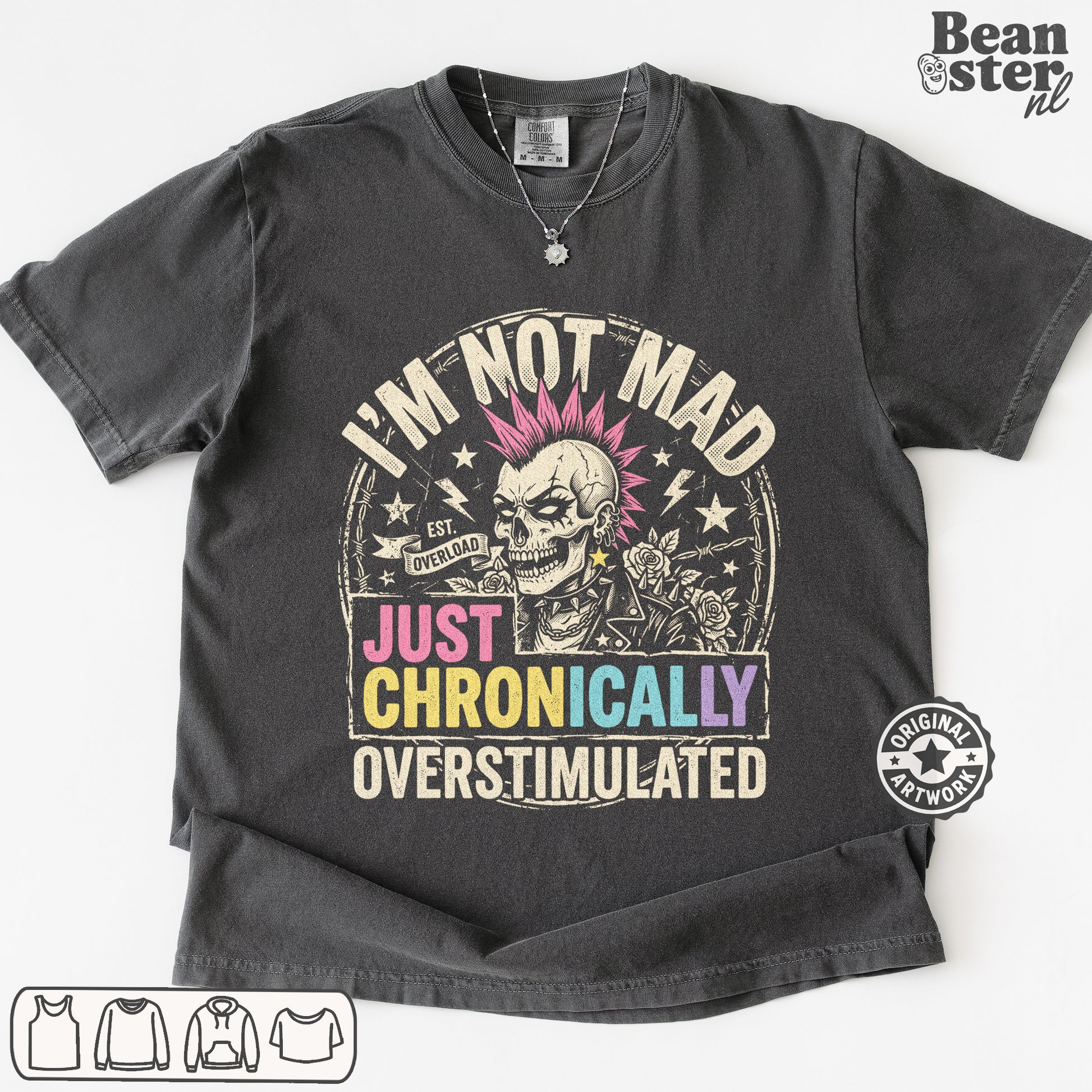 A dark gray graphic t-shirt featuring a skull with pink hair and the text 'I'M NOT MAD JUST CHRONICALLY OVERSTIMULATED'. 