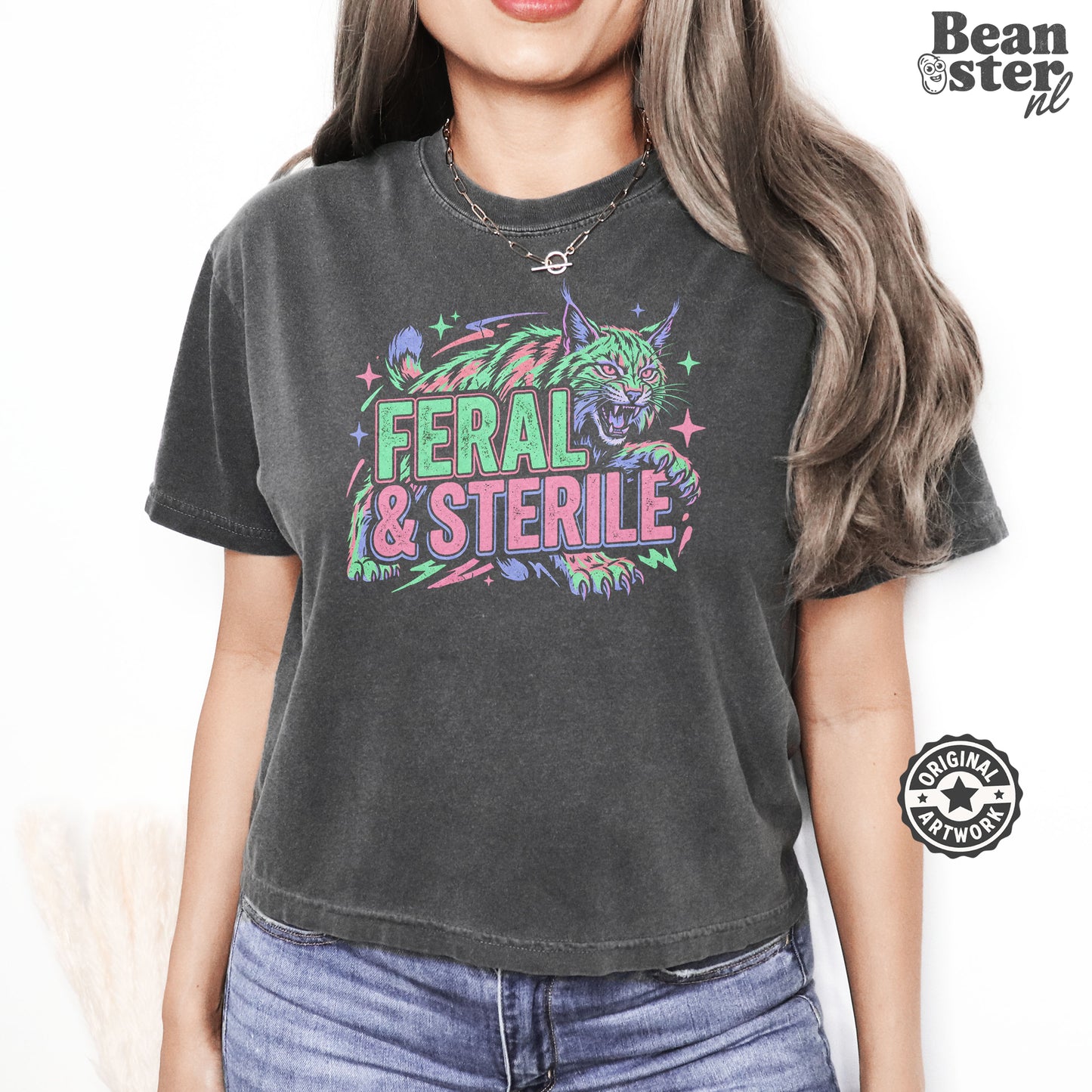 A woman wearing a dark gray washed graphic t-shirt with a colorful feral cat design and the text 'FERAL & STERILE'. The background is white with a Beanster.