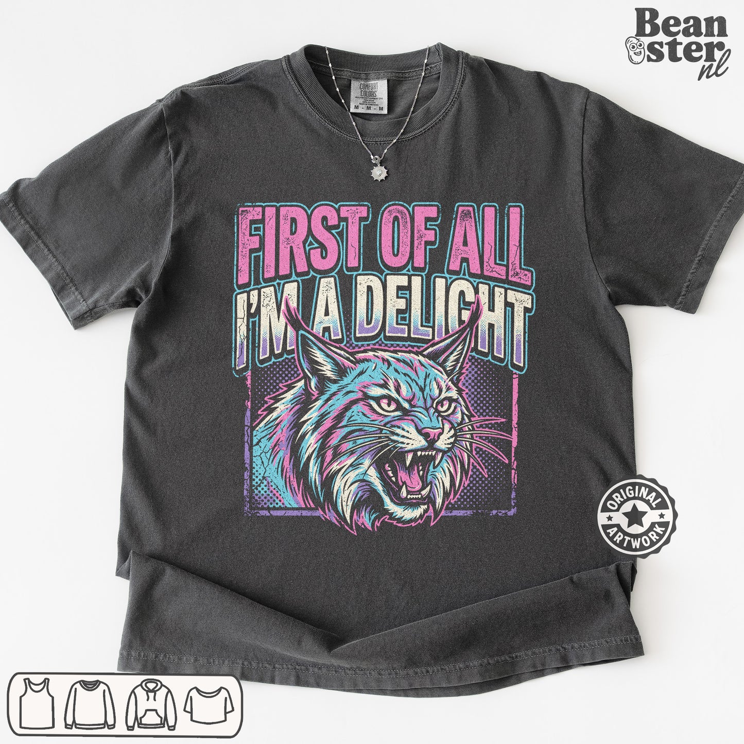 A dark gray graphic t-shirt featuring a stylized lynx cat illustration and the text 'FIRST OF ALL I'M A DELIGHT' in pink and teal. The t-shirt is displayed flat against a white background with a 'Beanster.