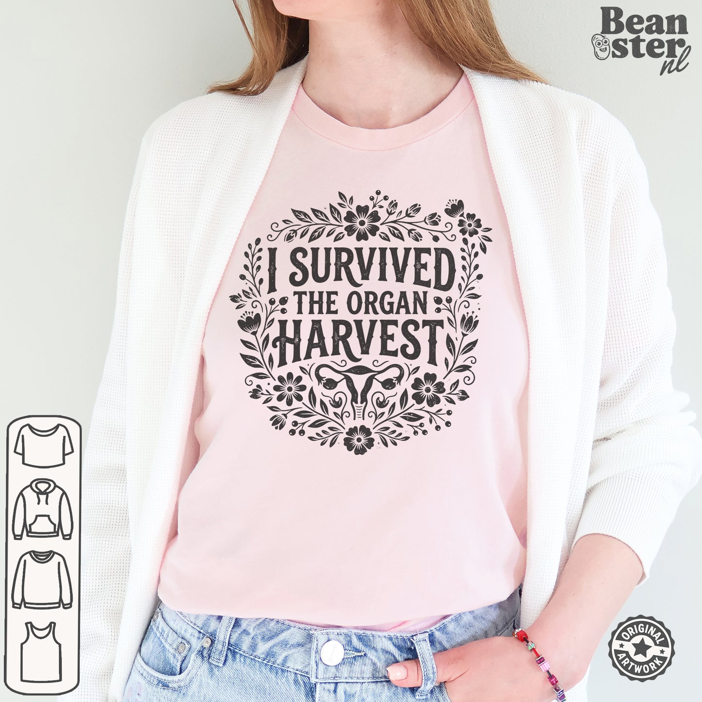 A woman wearing a light pink crewneck t-shirt with a black graphic print that reads 'I SURVIVED THE ORGAN HARVEST' surrounded by floral illustrations. She is wearing a white cardigan and blue jeans, with a 'Beanster.