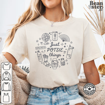 A woman wearing a cream-colored graphic t-shirt with a black line art design that reads 'Just POTSIE things' surrounded by small doodles. The image has a 'Beanster.