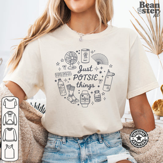 A woman wearing a cream-colored graphic t-shirt with a black line art design that reads 'Just POTSIE things' surrounded by small doodles. The image has a 'Beanster.