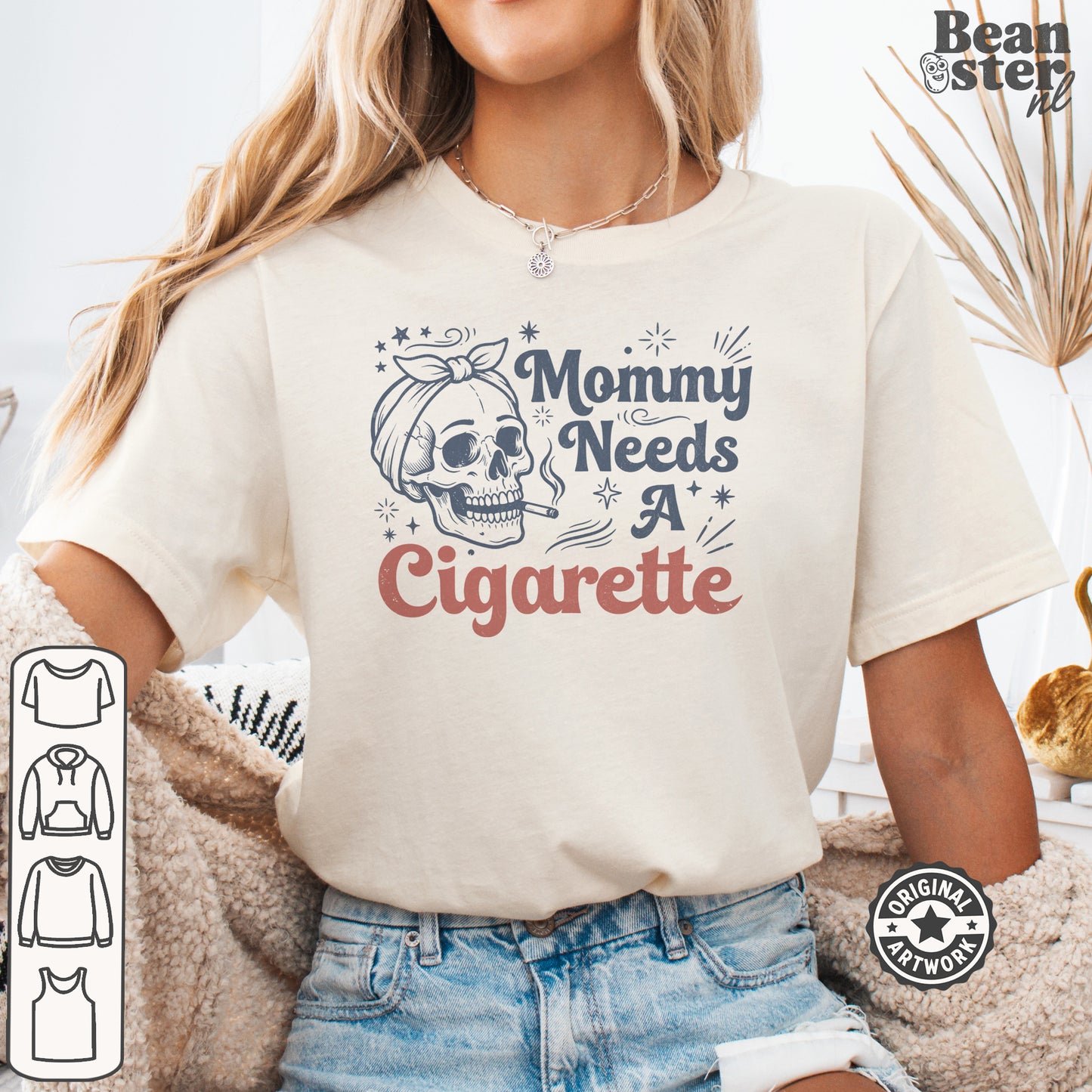 A woman wearing a cream-colored graphic t-shirt with a skull illustration and the text 'Mommy Needs A Cigarette' in navy and dusty pink. The image is a digital mockup with a 'Beanster.