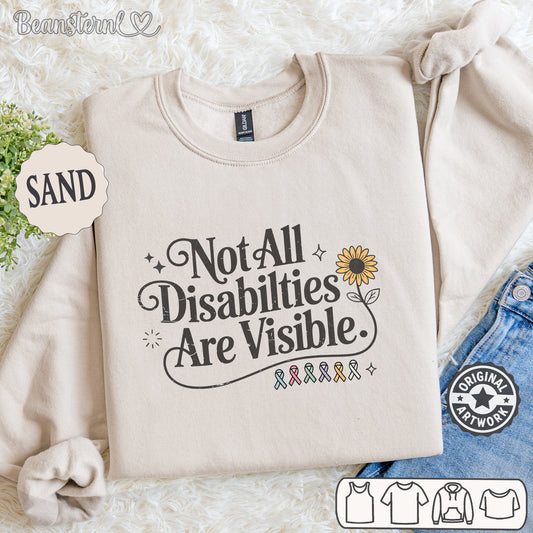 Beige sweatshirt with 'Not All Disabilities Are Visible' text and sunflower graphic on a textured surface.