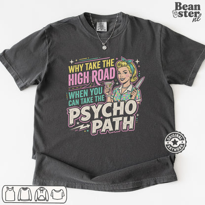 A dark charcoal gray graphic t-shirt laid flat on a white background. The shirt features a retro-style pin-up illustration of a woman with blonde hair and a headband, holding a drink, next to the text 'WHY TAKE THE HIGH ROAD WHEN YOU CAN TAKE THE PSYCHO PATH' in pink, yellow, and teal lettering.