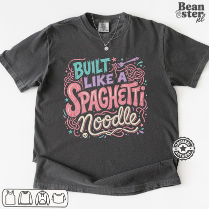 A dark gray graphic t-shirt featuring the text 'Built Like a Spaghetti Noodle' in stylized pink, purple, and teal lettering with pasta illustrations. The t-shirt is displayed flat against a white background with a 'Beanster.