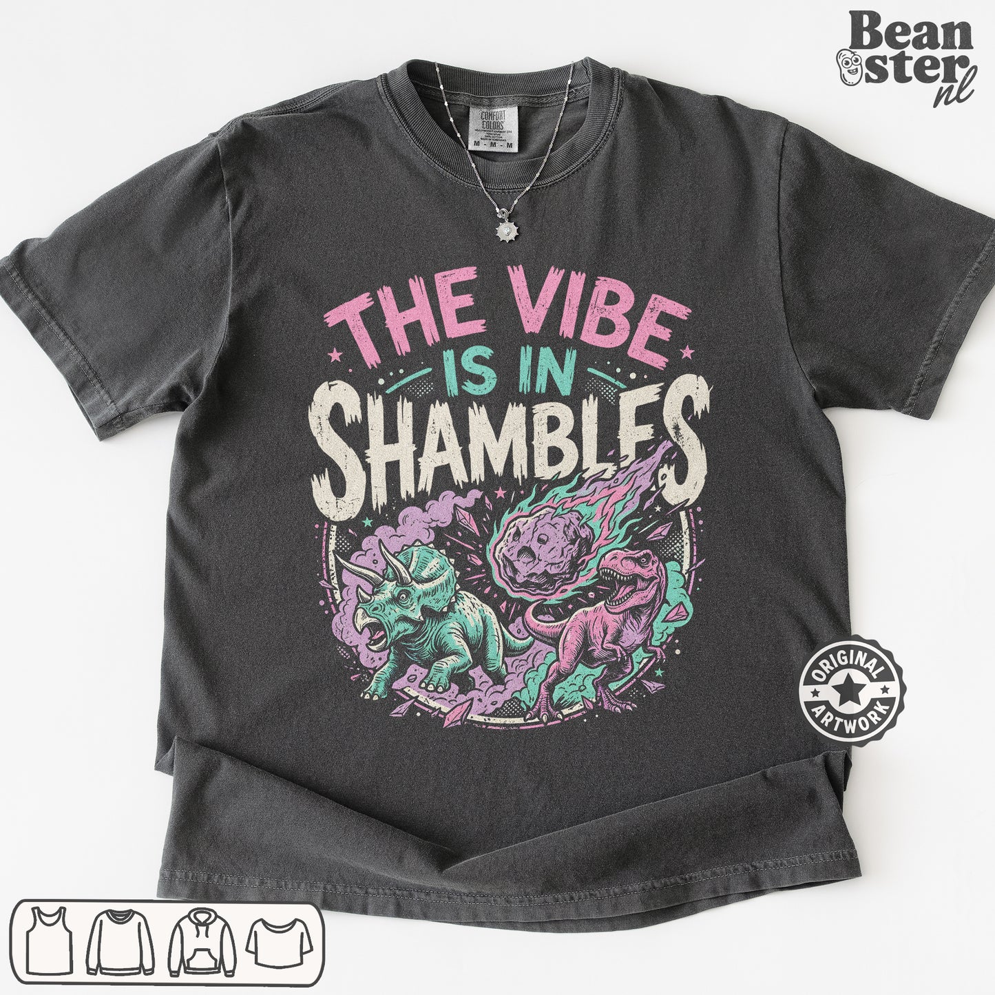 A dark charcoal gray graphic t-shirt laid flat on a white background. The shirt features a colorful print with the text 'THE VIBE IS IN SHAMBLFS' in pink, teal, and white, above an illustration of a purple and teal shambler dinosaur.