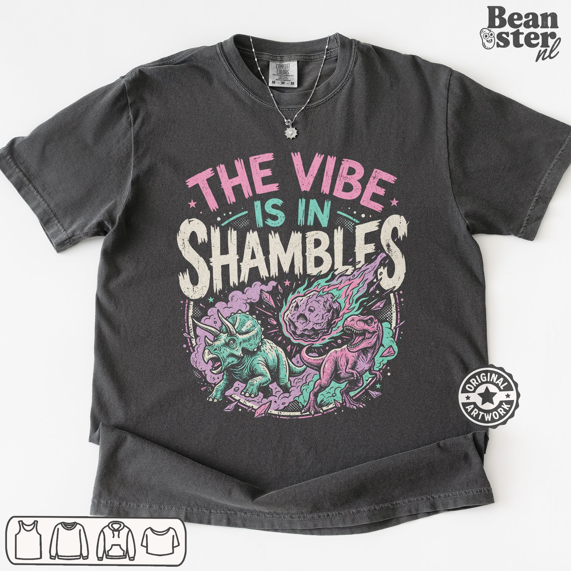 A dark charcoal gray graphic t-shirt laid flat on a white background. The shirt features a colorful print with the text 'THE VIBE IS IN SHAMBLFS' in pink, teal, and white, above an illustration of a purple and teal shambler dinosaur.
