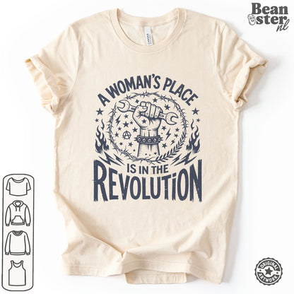 A beige short-sleeve t-shirt with a dark navy graphic print that reads 'A WOMAN'S PLACE IS IN THE REVOLUTION' surrounding a raised fist with a wrench and stars. 